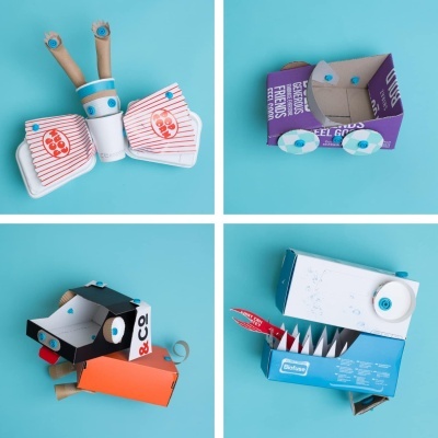 Montagem de quatro robôs feitos com caixas de cartão recicladas, copos e rolos, sobre fundo azul claro.