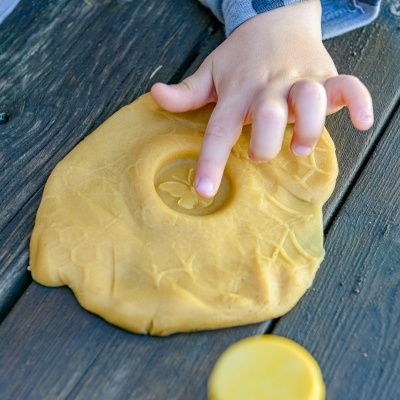 Massa de modelar amarela sendo moldada por mão de criança sobre madeira escura