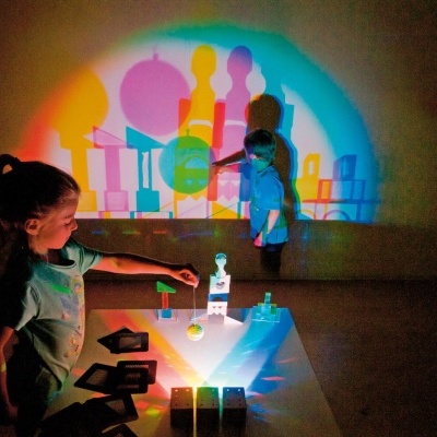 Crianças brincando com objetos translúcidos coloridos projetando sombras coloridas na parede