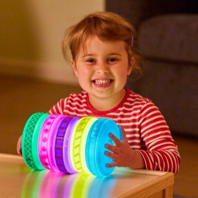 Criança com brinquedo luminoso de discos coloridos sobre mesa de madeira