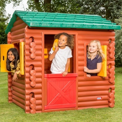 Casinha infantil de plástico castanha com telhado verde e porta vermelha com crianças ao redor.