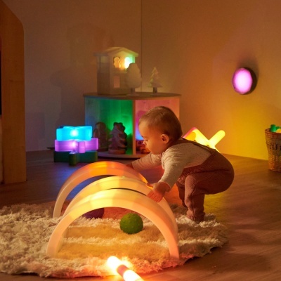 Bebé a jogar com arco de luzes coloridas num quarto com decoração luminosa e brinquedos de madeira.
