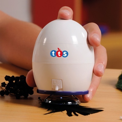 Dispositivo branco tts com base azul e cerdas pretas numa mesa de madeira com mão ao lado