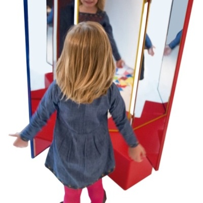 Criança a olhar para espelho triplo com molduras coloridas e base vermelha