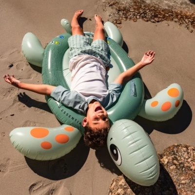 Rapazinho deitado numa bóia insuflável tartaruga na areia da praia.