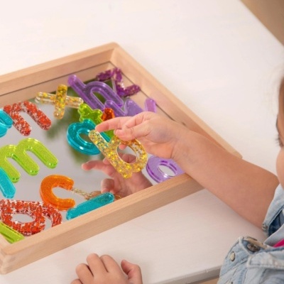 Letras do alfabeto coloridas em caixa de madeira, mão infantil a segurá-las