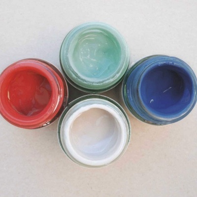 Quatro potes abertos com tinta de várias cores sobre uma superfície clara