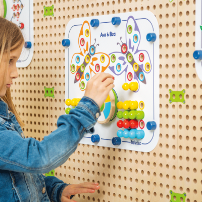 Criança usando painel educativo de madeira com botões coloridos fixado em parede perfurada