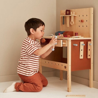 Criança a brincar com bancada de ferramentas de madeira em quarto claro