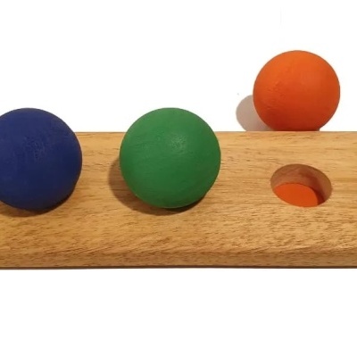 Tabuleiro de madeira com três bolas coloridas, azul, verde e laranja, em fundo branco