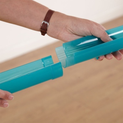 Mãos segurando tubo plástico azul-turquesa em duas partes encaixáveis, fundo de chão de madeira clara