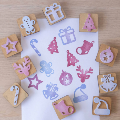 Carimbos de madeira com motivos de Natal em rosa e azul sobre mesa de madeira clara