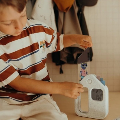 Criança com t-shirt às riscas e brinquedo digital em forma de casa com ecrã e figura de acrílico