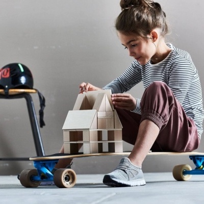 Criança a construir casa com blocos de madeira sentada em cima de skate