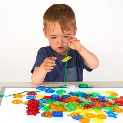 Criança a brincar com peças coloridas translúcidas numa mesa de luz