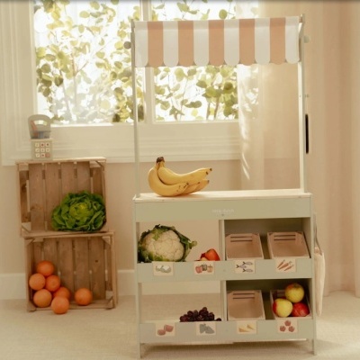 Carrinho de madeira para frutas e legumes com toldo rosa e branco em ambiente luminoso