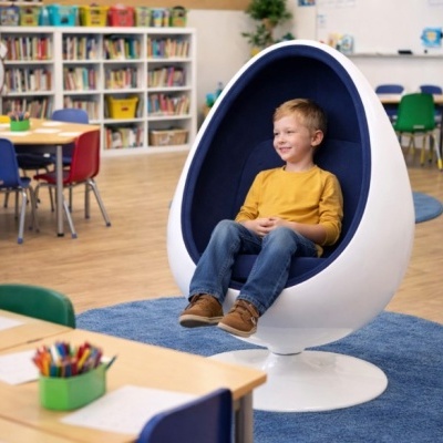 Criança numa cadeira de ovo branca com interior azul escuro numa sala de aula