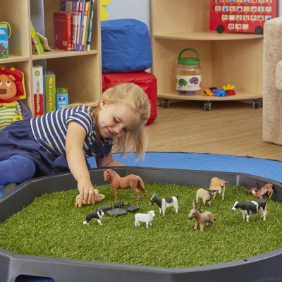 Menina a brincar com animais de plástico num tabuleiro com relva artificial