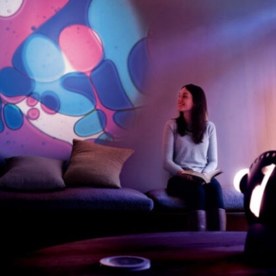 Sofá cinzento com almofadas e mulher a ler sob luzes coloridas projetadas