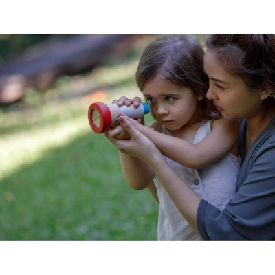 Criança a segurar brinquedo tubular colorido com ajuda de adulto num jardim