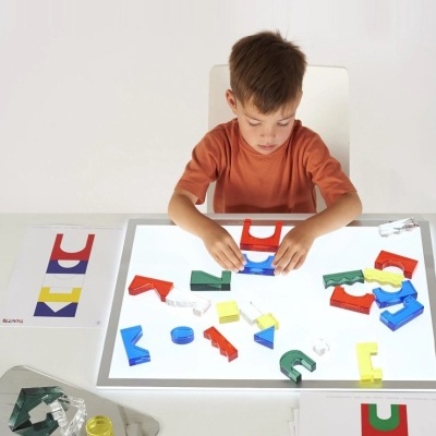 Criança a brincar com peças coloridas translúcidas numa mesa iluminada