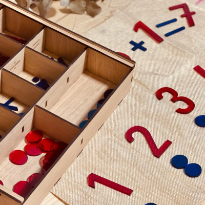 Jogo educativo de números vermelhos e fichas coloridas em tabuleiro de tecido claro com caixa organizadora de madeira