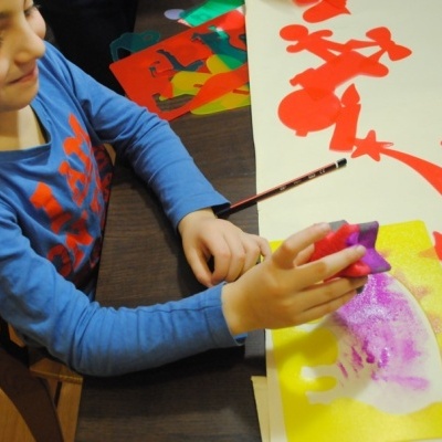 Criança a pintar com esponja em papel amarelo numa mesa com recortes coloridos