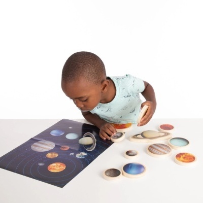 Criança com brinquedo educativo de planetas de madeira e cartaz do sistema solar.