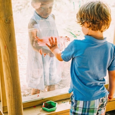 Criança a pintar numa superfície transparente com outra criança do outro lado