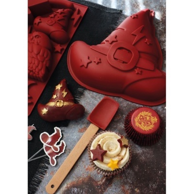 Forma de silicone vermelha em formato de bota de bruxa e cupcakes decorados sobre superfície escura.