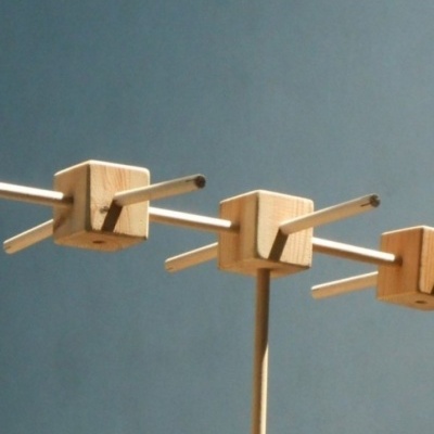 Ganchos de parede de madeira clara com braços metálicos sobre fundo azul.