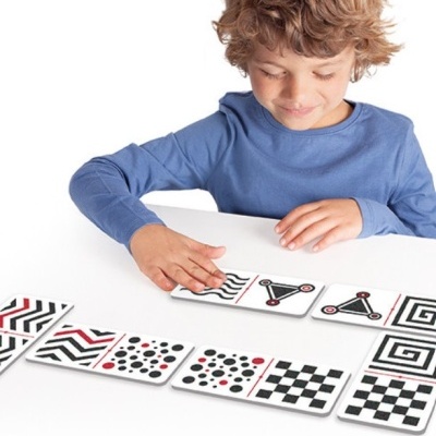 Criança mexendo em cartas com padrões geométricos em branco, preto e vermelho sobre mesa branca