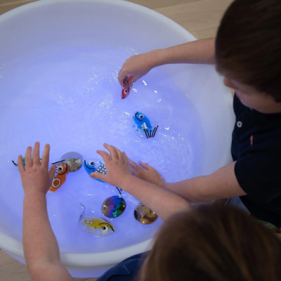 Crianças a brincar com peixes de brinquedo numa tina branca