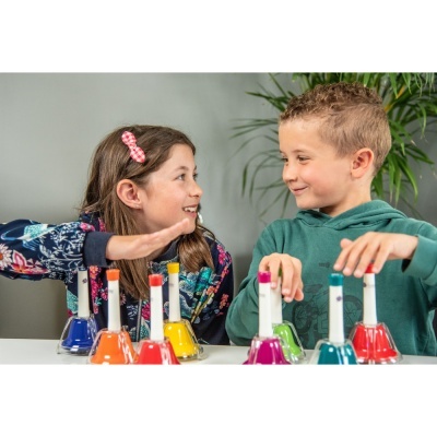 Crianças a tocar sinos coloridos sobre mesa branca