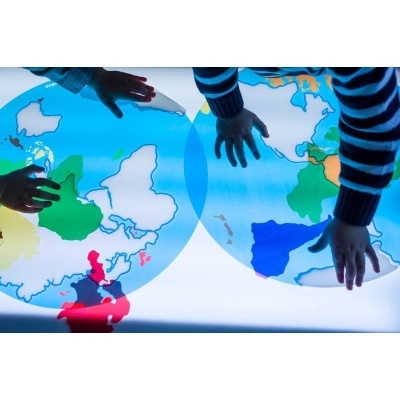 Mãos de crianças a tocar num mapa-múndi iluminado colorido.