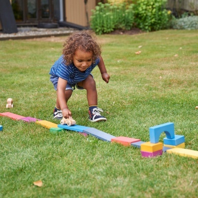 Criança a brincar com blocos coloridos e carro de madeira no relvado