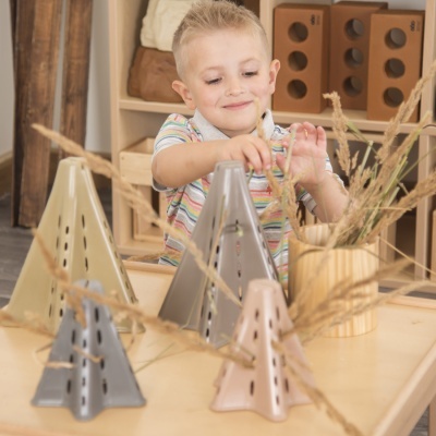 Quatro incensários de cerâmica triangulares coloridos numa mesa com vaso e criança ao fundo