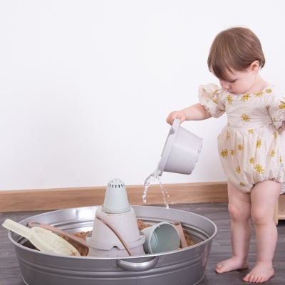 Criança a brincar com brinquedos de areia numa bacia metálica