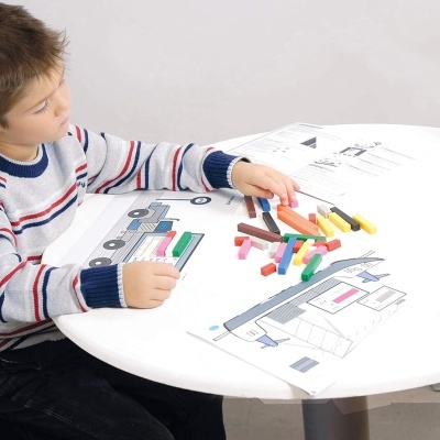 Menino a colorir desenhos técnicos numa mesa branca redonda com lápis de cor.