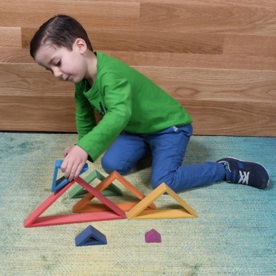 Menino a brincar com blocos de madeira triangulares coloridos no chão de um quarto com parede de madeira