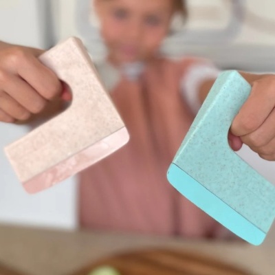 Duas espátulas texturizadas azul claro e bege com rosa claro, mãos segurando, fundo com tábua de cortar