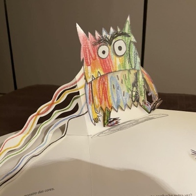 Livro pop-up com personagem colorido em papel recortado com padrão de arco-íris