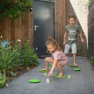 Crianças a brincar com discos verdes num caminho entre jardim e muro