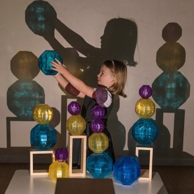 Criança a empilhar esferas coloridas translúcidas com suportes de madeira