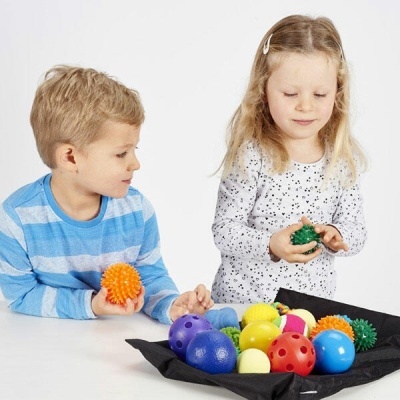 Duas crianças a brincar com bolas coloridas de várias texturas sobre mesa branca