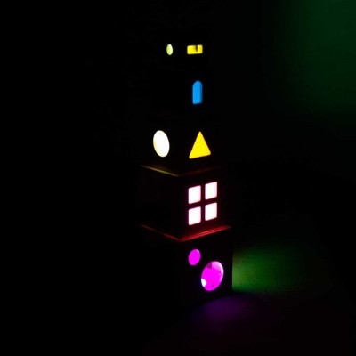 Torre iluminada com blocos geométricos coloridos em fundo escuro