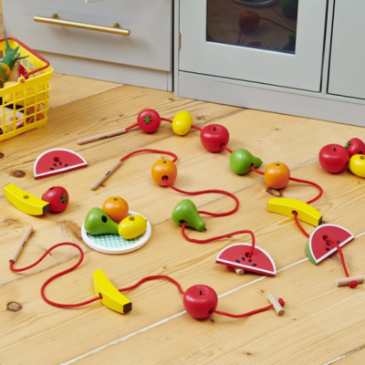 Brinquedo de madeira de frutas para enfiar em cordão sobre superfície de madeira com armários de cozinha ao fundo