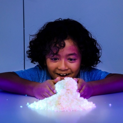 Criança com cabelo encaracolado brinca com flocos brancos brilhantes sobre superfície azul