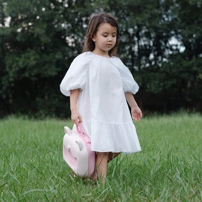 Criança com vestido branco e mochila rosa em forma de coelho na relva