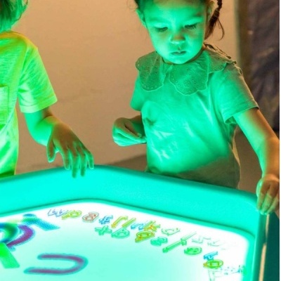 Criança a interagir com mesa luminosa azul e letras coloridas